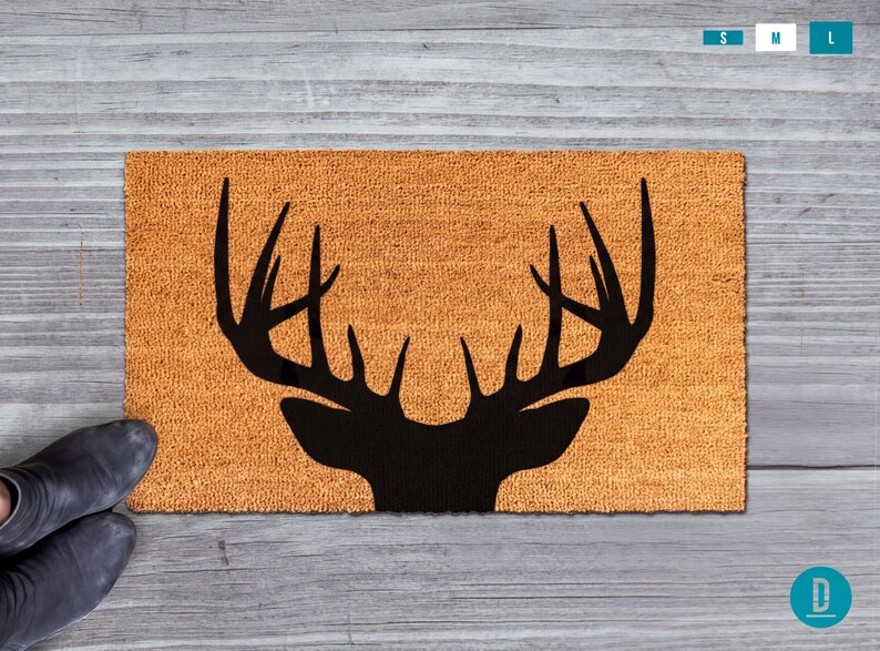A pair of black boots is positioned next to a wooden surface with a decorative orange mat featuring a black silhouette of a deer's head.