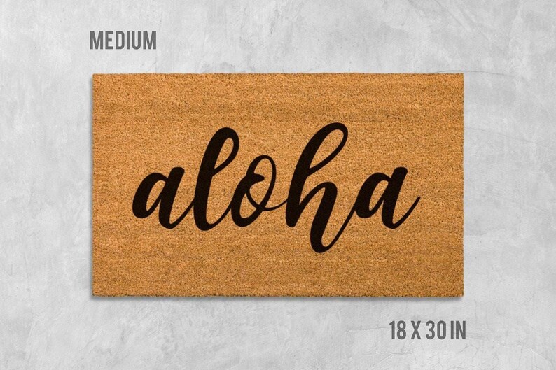 A rectangular, light brown, textured doormat with the word "aloha" written on it in a cursive font.