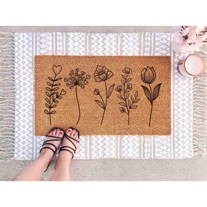 A pair of feet standing on a decorative mat with a floral design, along with a small vase of flowers and a candle.