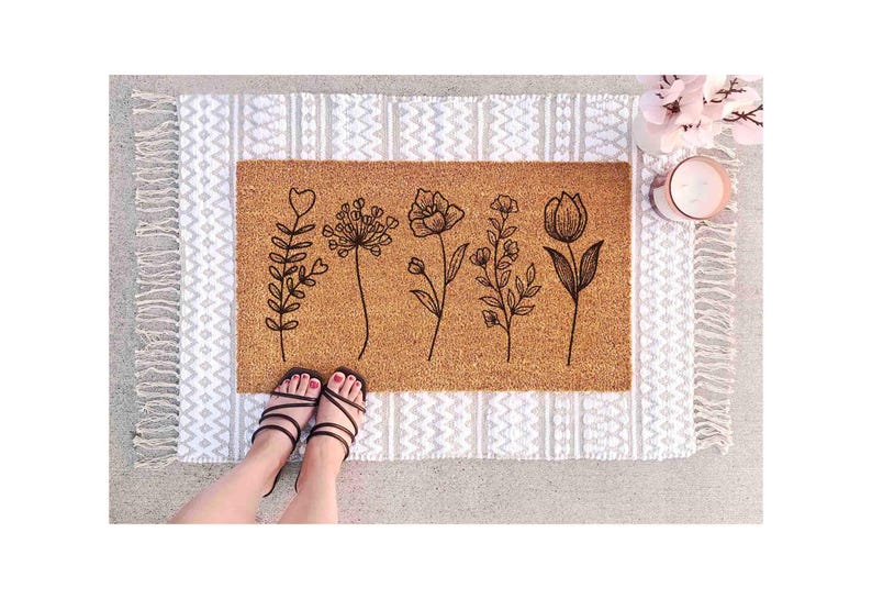 A pair of feet standing on a decorative mat with a floral design, along with a small vase of flowers and a candle.