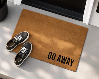 May include: A rectangular brown coir doormat with the text GO AWAY printed in bold black capital letters. A pair of black low-top sneakers with white laces and white rubber soles are placed on the left side of the mat.