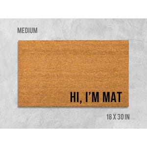 a rectangular, light brown, textured door mat with the text "Hi, I'm MAT" printed on it.
