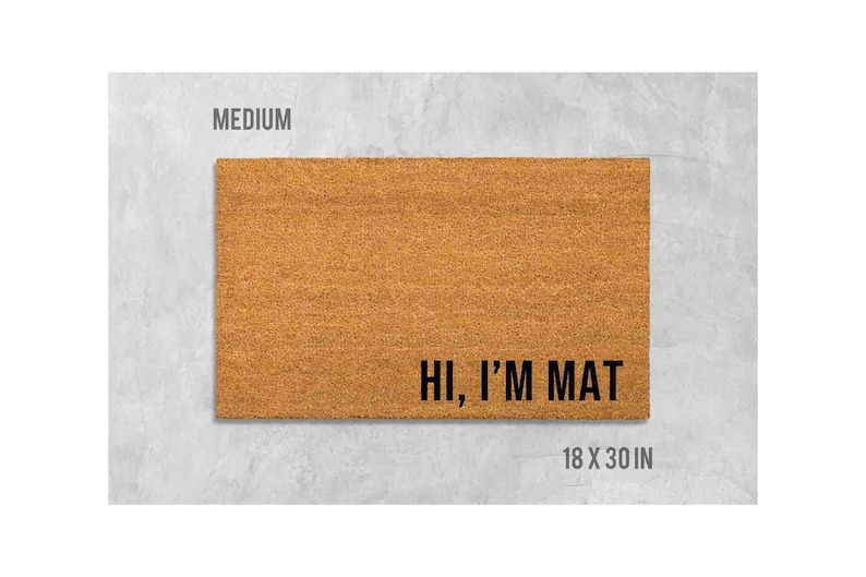 a rectangular, light brown, textured door mat with the text "Hi, I'm MAT" printed on it.