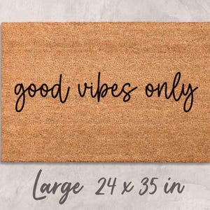 A rectangular, light brown, textured doormat with the text "good vibes only" printed on it.