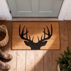 A wooden door with a mat featuring a deer head silhouette, a woven basket, and a potted plant on the floor.