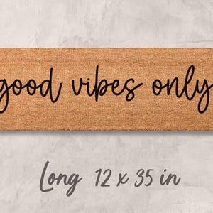 A rectangular wooden door mat with the text "good vibes only" written on it.