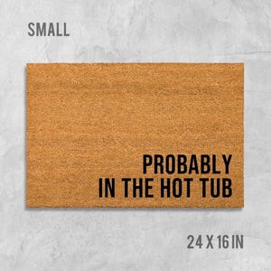 A rectangular, light brown, textured doormat with the text "Probably in the hot tub" printed on it.