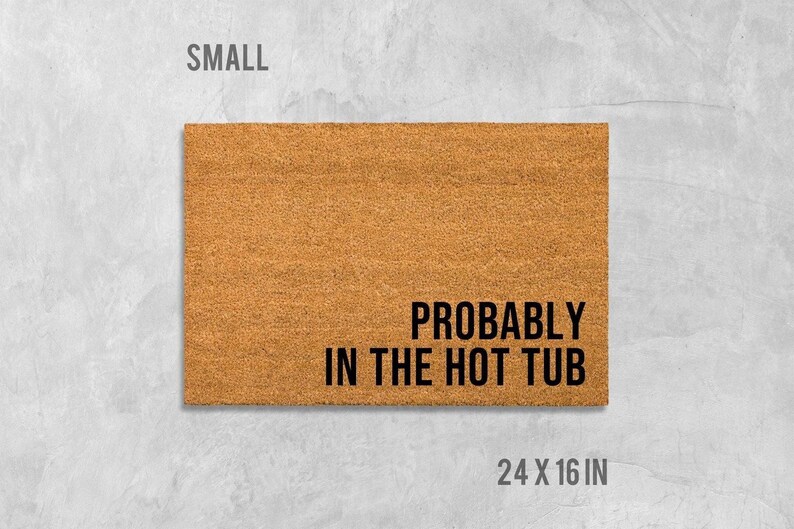 A rectangular, light brown, textured doormat with the text "Probably in the hot tub" printed on it.