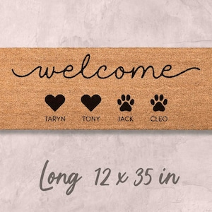 A wooden door mat with the word "welcome" written on it, along with four heart symbols and four paw prints. The mat is described as being long, 12 x 35 inches in length.