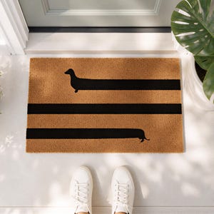 A pair of white sneakers is positioned on a mat with a black and orange design, featuring a dachshund silhouette.