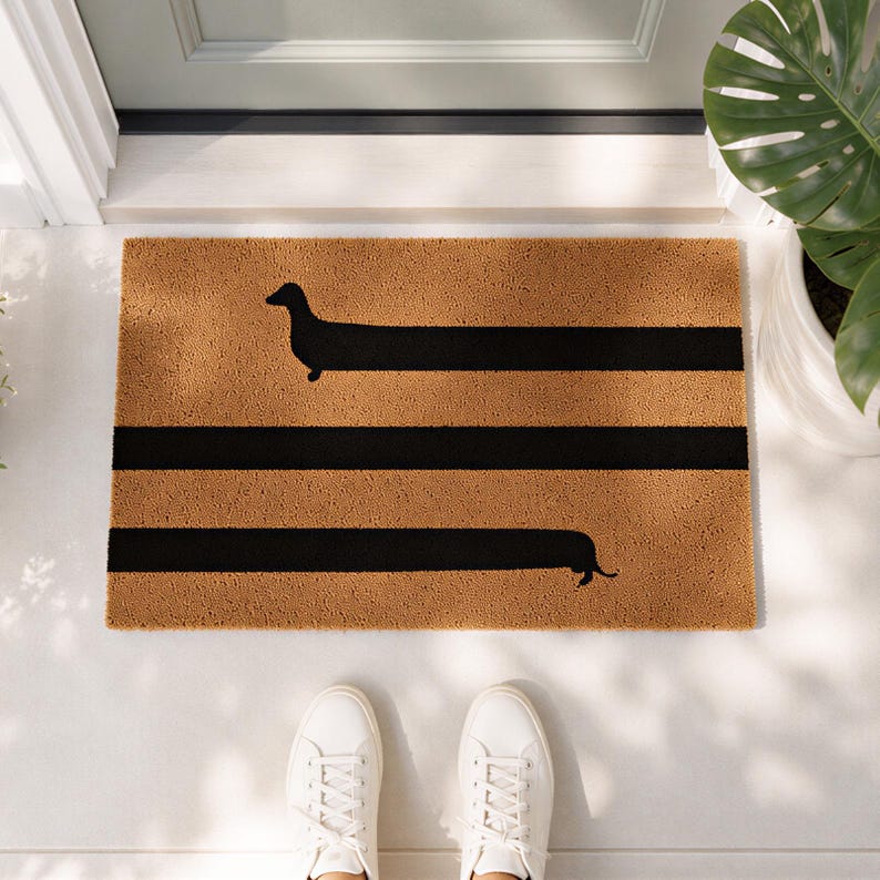 A pair of white sneakers is positioned on a mat with a black and orange design, featuring a dachshund silhouette.