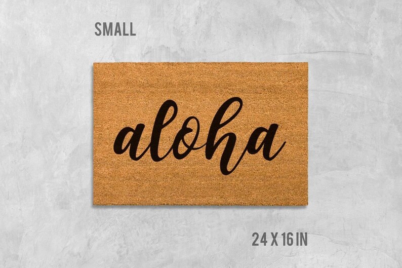 A rectangular, light brown, textured doormat with the word "aloha" written on it in a cursive font.