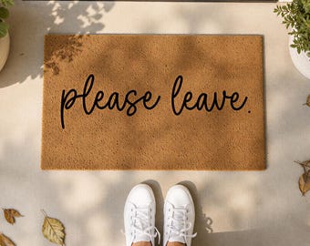 Puede incluir: Un felpudo rectangular de fibra de coco color canela con el texto please leave. escrito en una fuente cursiva negra. La alfombra tiene una textura fibrosa y rugosa y está colocada sobre una superficie plana, centrada en el encuadre.