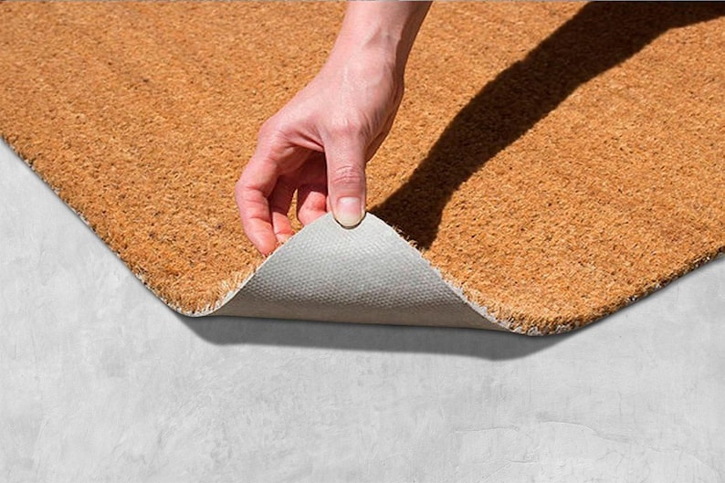 A hand is holding a piece of a cork or natural fiber mat, which is being stretched out on a concrete surface.