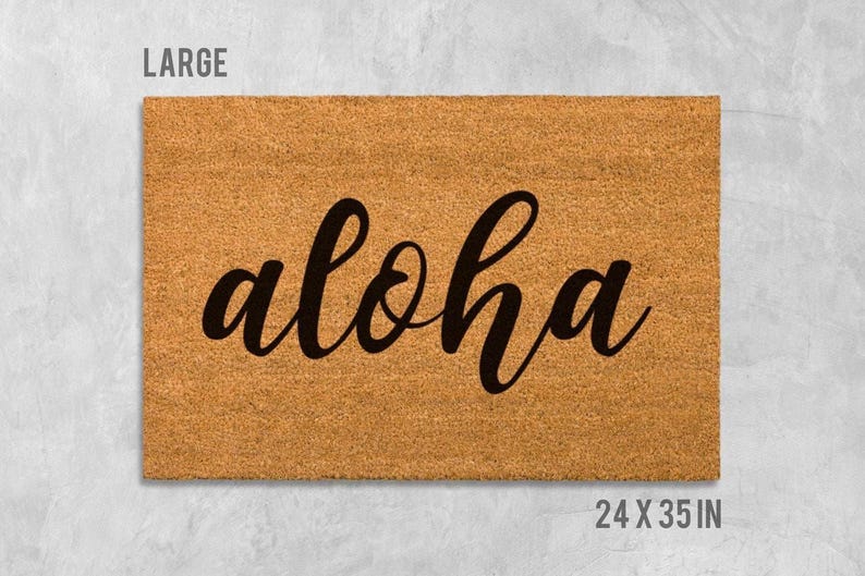 A large, rectangular, beige-colored doormat with the word "aloha" written on it in a cursive font.