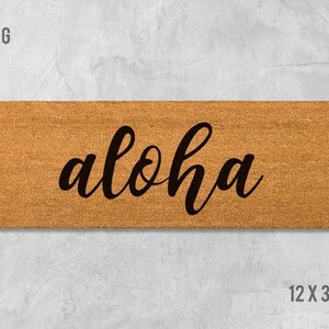 A rectangular wooden door mat with the word "aloha" written on it in a cursive font.