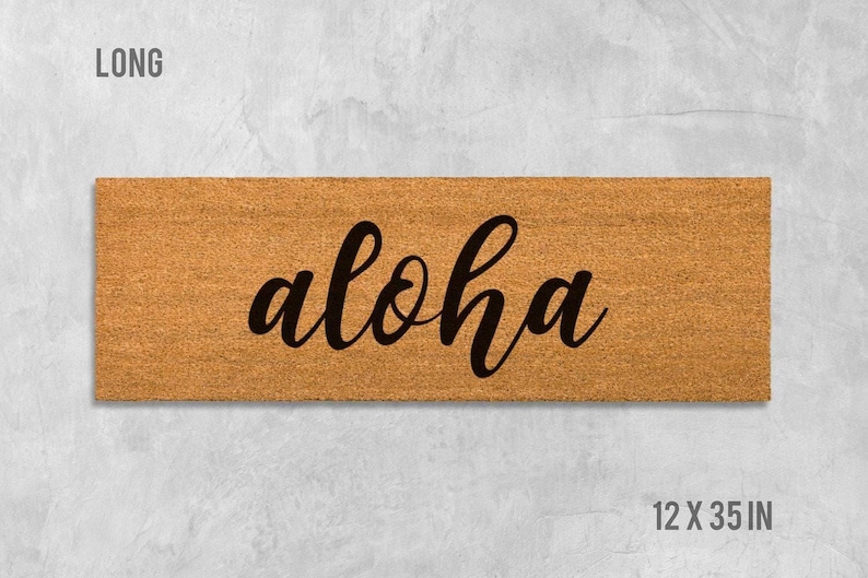 A rectangular wooden door mat with the word "aloha" written on it in a cursive font.