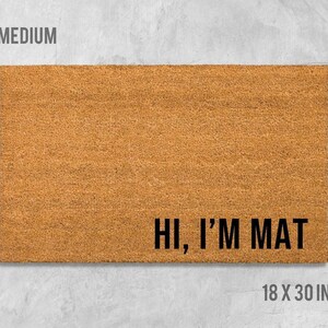 A rectangular, light brown, textured doormat with the text "Hi, I'm MAT" printed on it.