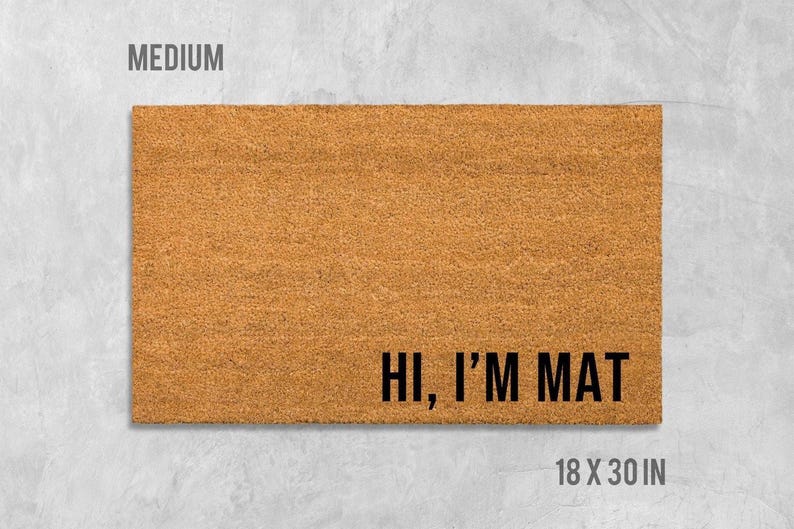 A rectangular, light brown, textured doormat with the text "Hi, I'm MAT" printed on it.