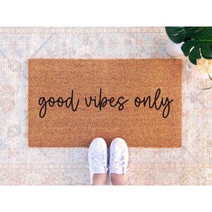 A pair of white sneakers stands on a patterned rug with the phrase "good vibes only" written on it.