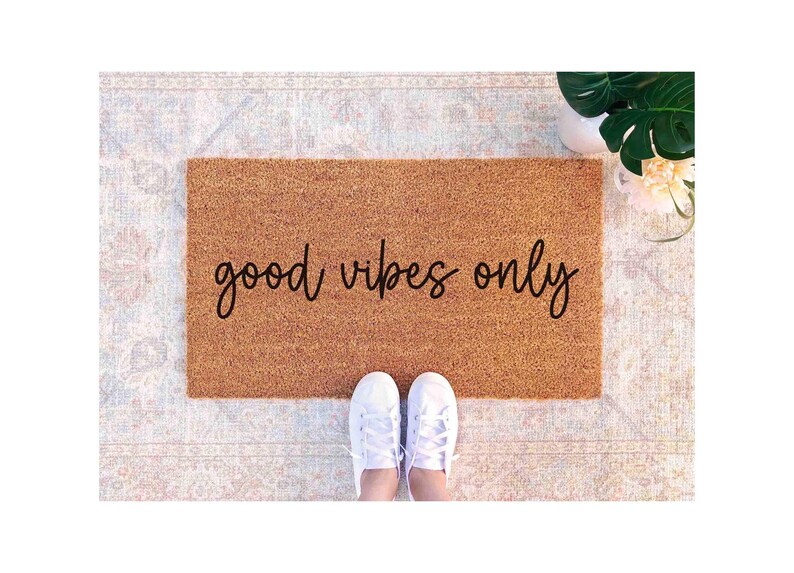 A pair of white sneakers stands on a patterned rug with the phrase "good vibes only" written on it.