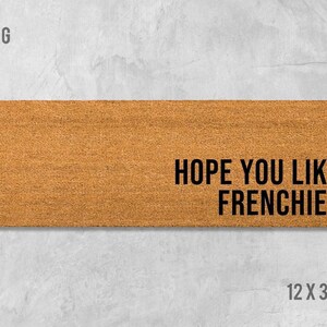 a rectangular, brown, textured doormat with the text "HOPE YOU LIKE FRENCHIES" printed on it.