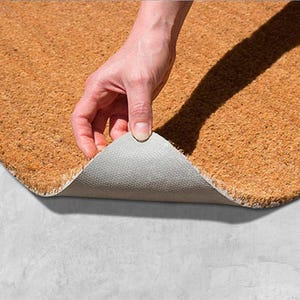 A hand is holding a piece of a cork or natural fiber mat, which is being stretched out on a concrete surface.