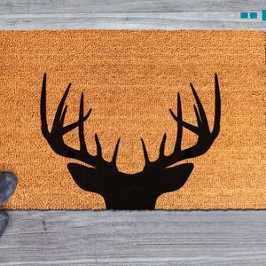 A pair of black boots is placed next to a brown, textured area rug with a black silhouette of a deer's head.