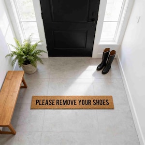 a wooden bench, a black door, a potted plant, and a mat with the text "PLEASE REMOVE YOUR SHOES" on it.