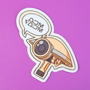 Op de afbeelding: Een witte sticker met een cartoonillustratie van een gele robot met één oog en een spraakballon die "DOOM FOOM" zegt.