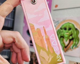 May include: Pink keychain with a cityscape design and the text "NFKDV" printed on it.