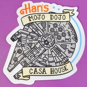 May include: A white sticker with a black and gray illustration of the Millennium Falcon spaceship. The sticker has a yellow banner with the text "Han's Mojo Dojo Casa House".