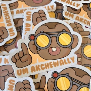 May include: A collection of stickers featuring a cartoon character with brown skin, round yellow-tinted glasses, and a single tooth. The character is pointing with a finger, and the text "UM AKCHEWALLY" is printed on the sticker.