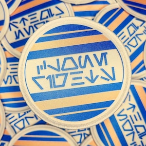 May include: A close-up of a round, blue and white striped patch with the text "NAVI" in a stylised font. The patch has a white border and is surrounded by other similar patches.