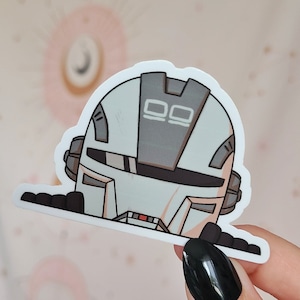May include: A white and gray robot sticker with a black visor and two squares on the top of its head. The robot is peeking over a white surface.