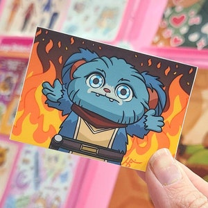 May include: A blue and brown cartoon character with large eyes and a worried expression is surrounded by flames. The character is wearing a brown sash and a black belt.