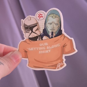 Puede incluir: Una pegatina troquelada con un casco de soldado clon blanco y un personaje de piel pálida con capucha azul dentro de una camiseta naranja. La camiseta tiene el texto OUR "GETTING ALONG" SHIRT en blanco y un símbolo rojo de enfado.