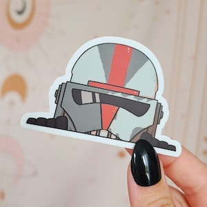 Könnte beinhalten: Ein weißer und roter Cartoon-Aufkleber eines Star Wars Klon-Soldaten mit schwarzem Visier. Der Aufkleber befindet sich auf weißem Hintergrund.