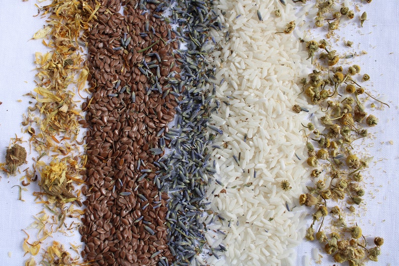 May include: Four rows of different dried ingredients, including yellow calendula petals, brown flax seeds, purple lavender buds, and white rice.