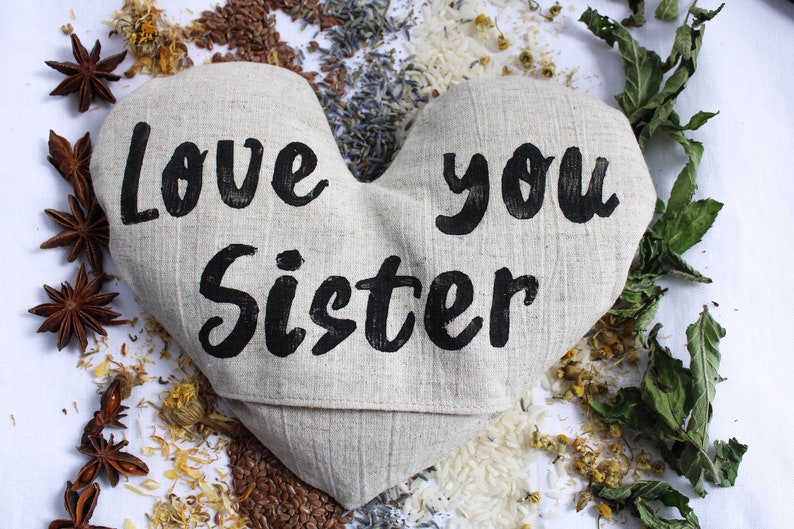 May include: A heart-shaped linen pillow with the words "Love you Sister" printed in black. The pillow is surrounded by dried herbs and flowers.