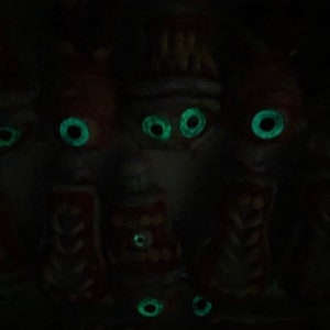 May include: A group of five small, dark figures with glowing green eyes. The figures are made of a dark material and have a slightly creepy appearance.