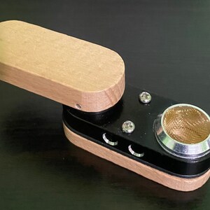 May include: A small wooden and black pipe with a metal bowl and a screen. The pipe has a hinged lid and three small holes on the side.