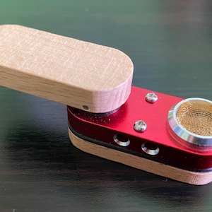 May include: A small, wooden and red metal pipe with a screen on the end. The pipe has a hinged lid and a small hole on the side.