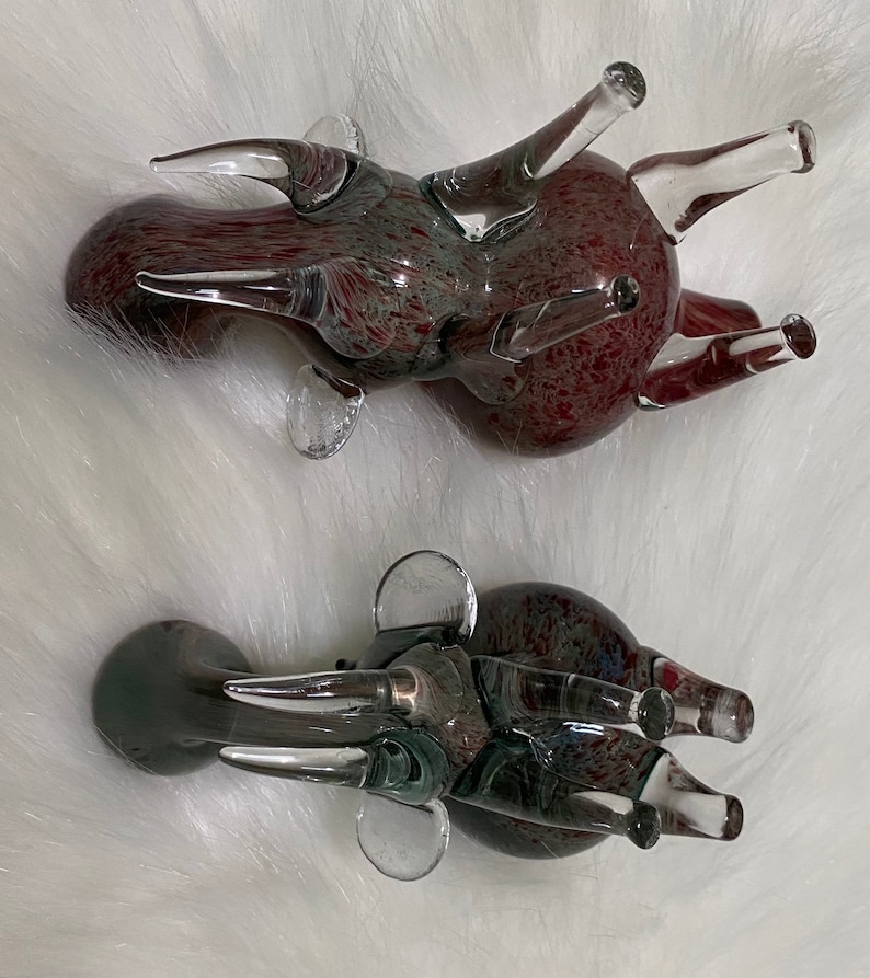 Op de afbeelding: Twee glazen dierenfiguren, een rood en een grijs, met een gespikkelde afwerking. Beide hebben lange, dunne poten en een rond lichaam.
