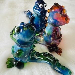 May include: Three glass dragon figurines with blue, green, and purple iridescent paint. The dragons have large eyes and are in a playful pose.