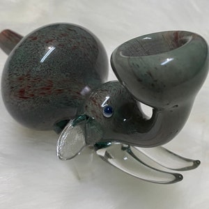Op de afbeelding: Een grijze glazen olifantenpijp met rode en witte swirls. De pijp heeft een ronde kom en een lange, gebogen tuit. Het oog van de olifant is een blauwe glazen kraal.