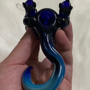 May include: A blue and black glass pipe shaped like a dragon with a bowl on its back and a long tail.