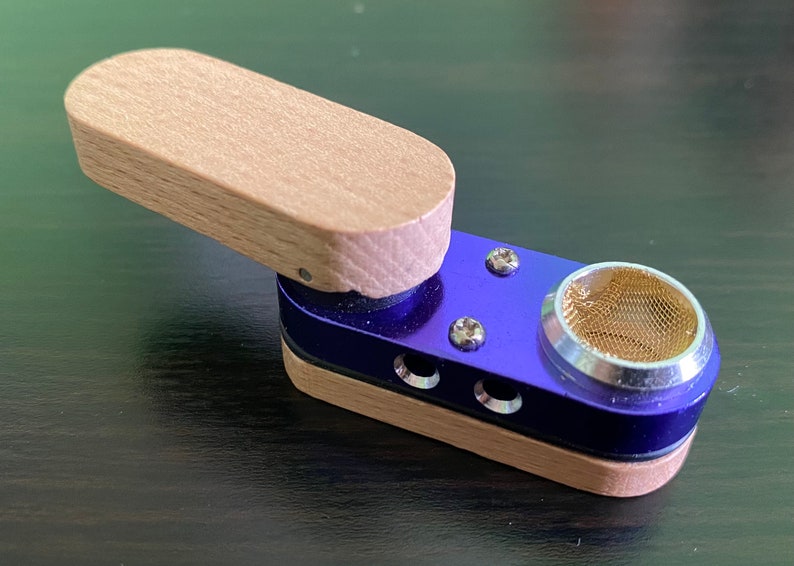 May include: A small, portable wooden and metal smoking pipe with a blue metal body and a wooden lid. The pipe has a mesh screen and a small hole for airflow.