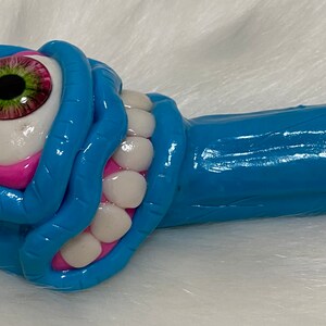May include: A blue and pink ceramic pipe with a single large eye and a row of teeth. The pipe has a white tip.