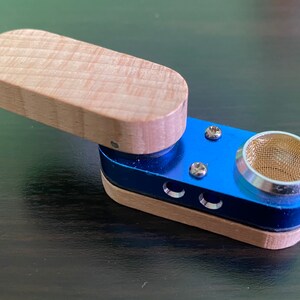 May include: A small, blue and wood smoking pipe with a metal screen. The pipe has a removable wooden lid.